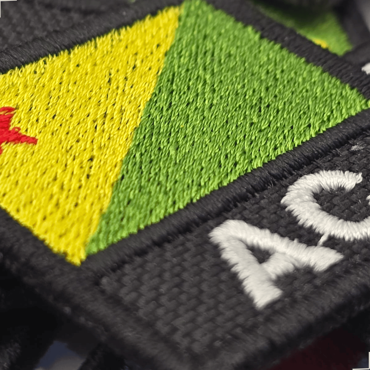 Detalhe do patch bordado da bandeira do Acre com sigla AC e contorno preto