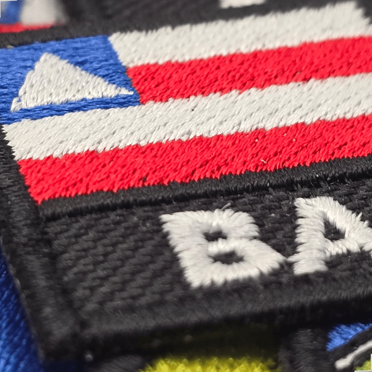 Detalhe do patch bordado da bandeira da Bahia com sigla BA e acabamento preto