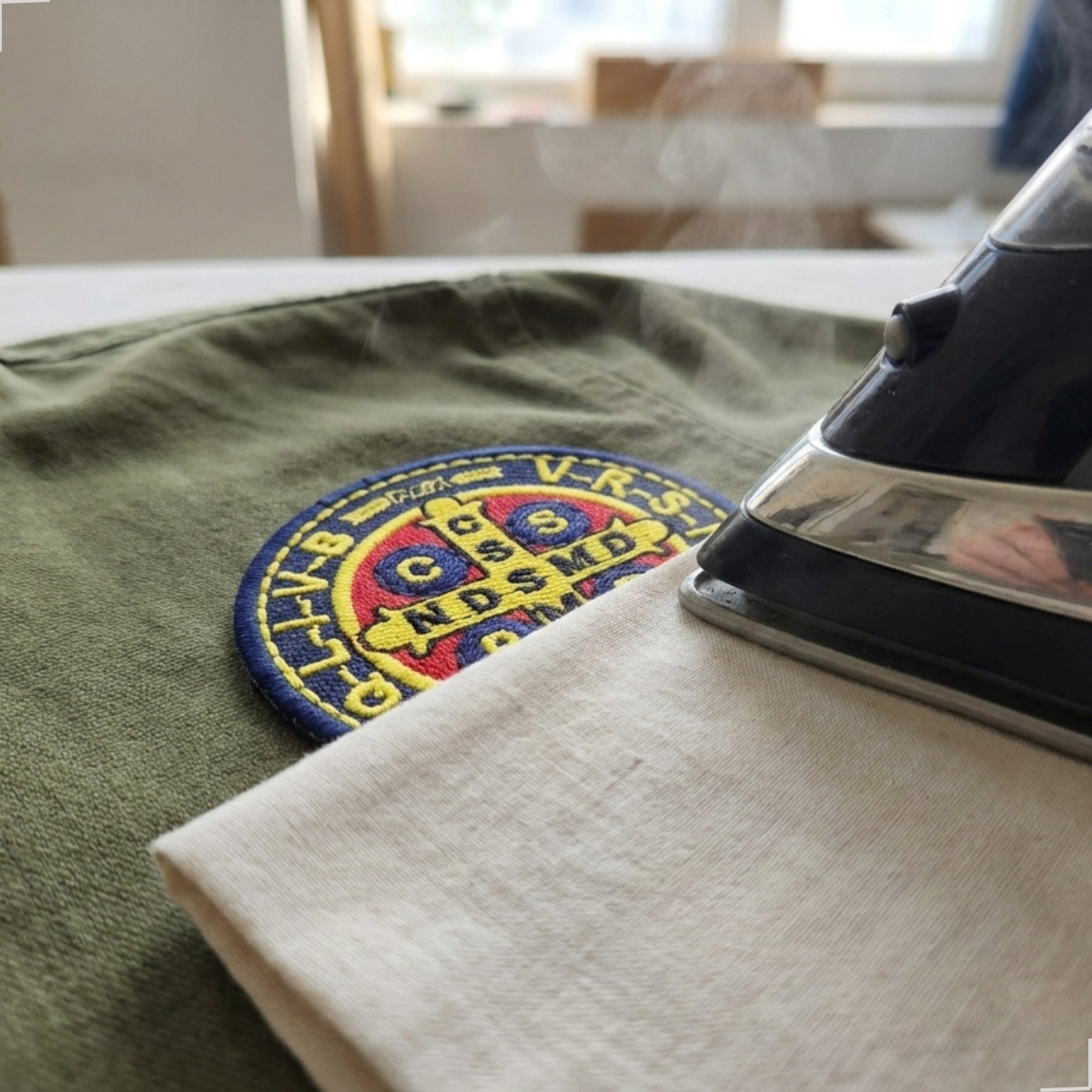Aplicação do patch termocolante Medalha de São Bento com ferro e tecido de proteção