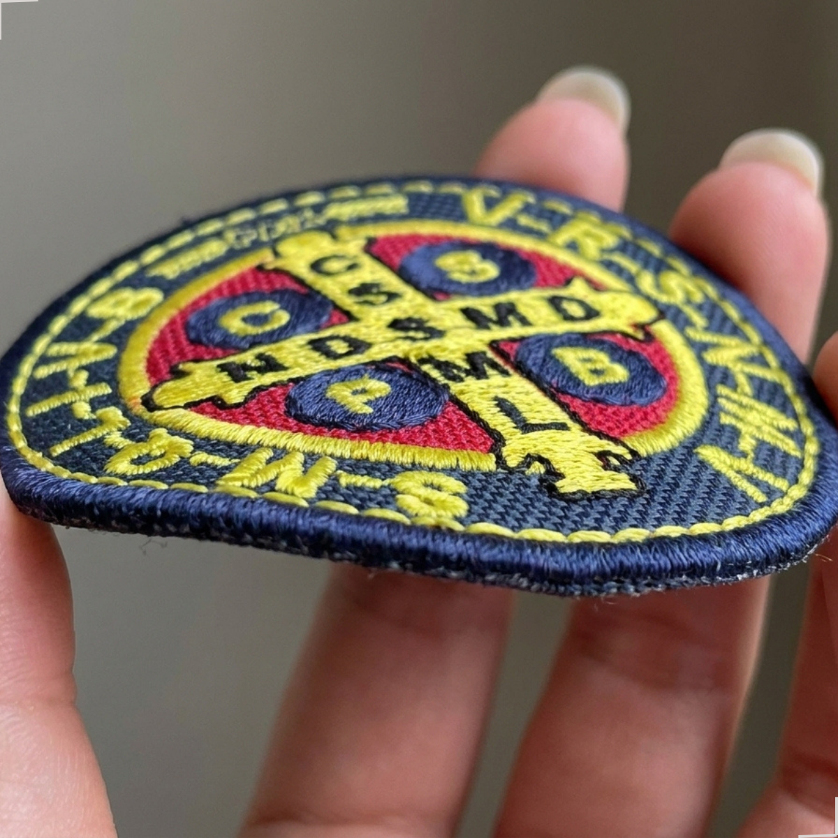 Patch Medalha de São Bento segurado de lado, mostrando espessura e acabamento da borda bordada